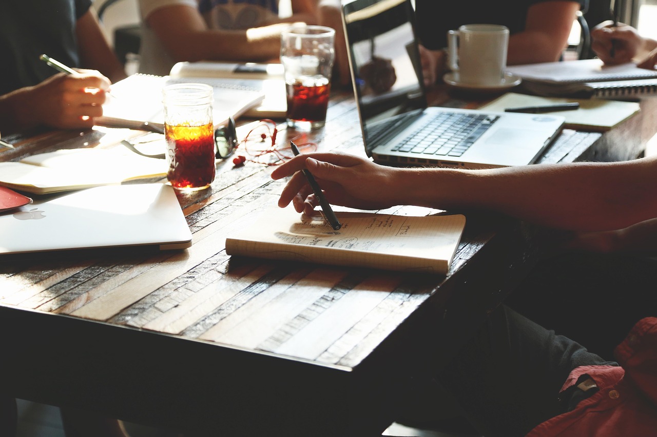 Three people around a laptop at a cafe table, planning an online income stream while still employed